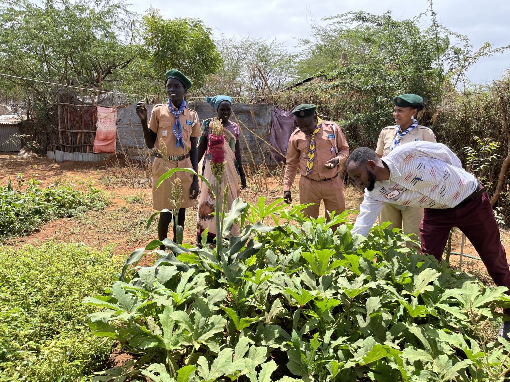 Far left, Kok Matip, a South Sudan refugee in Kenya, Dadaab Camp, showing the kitchen garden he maintains at home thanks yo the skills gained from the Food for Life initiative with the scouts. 