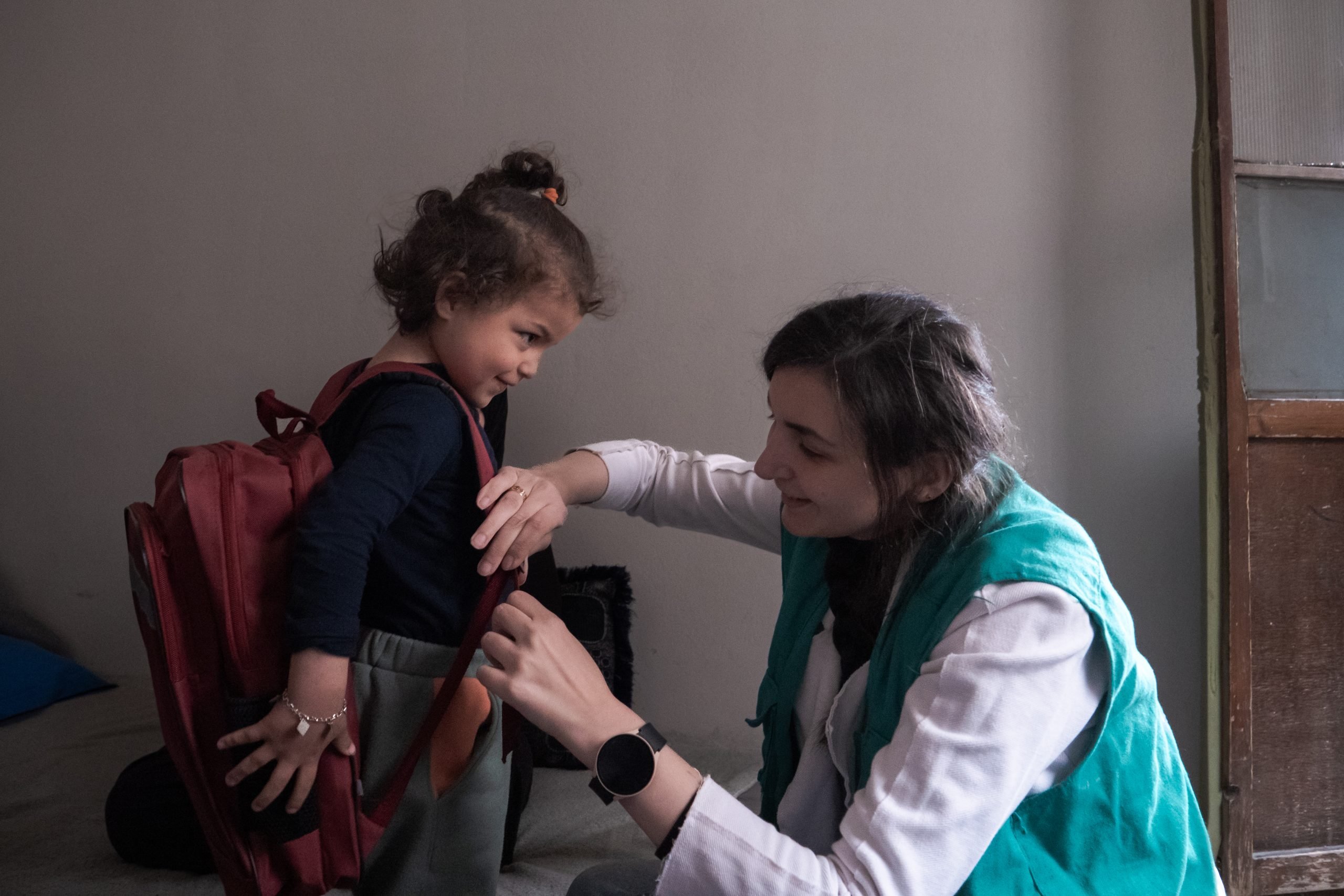 Un'operatrice di AVSI aiuta la secondogenita di Wafa a indossare uno zainetto Siria